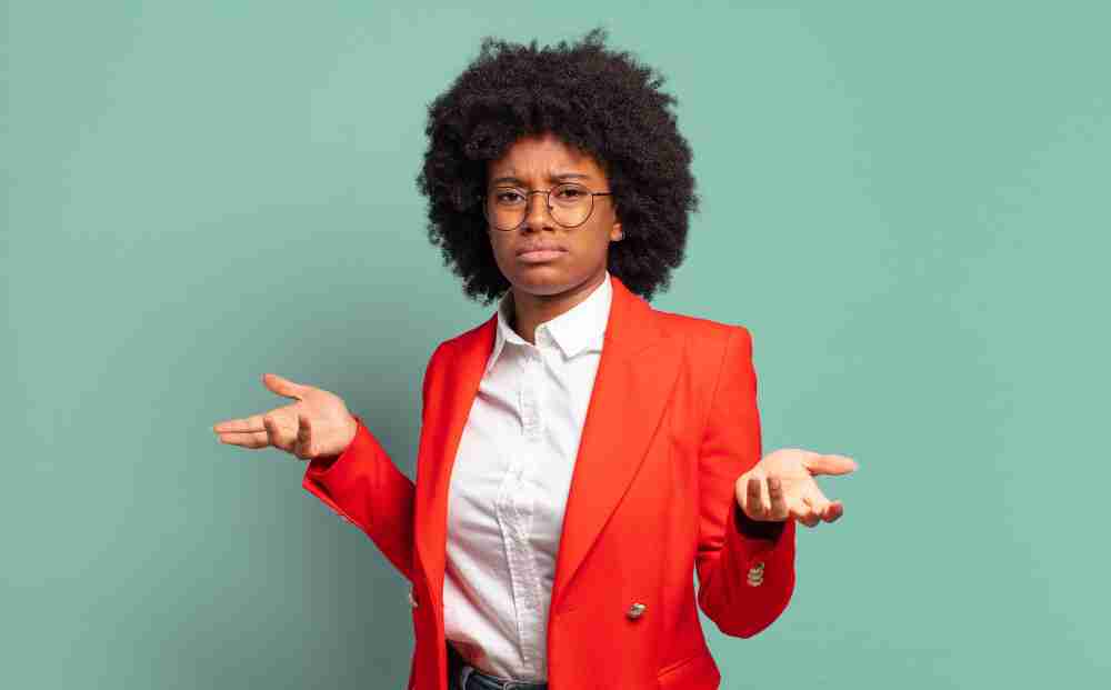 When Is On-Demand Consulting the Right Fit Person with curly hair and glasses wearing a red blazer, standing against a mint green background, gesturing with both hands in a questioning manner.